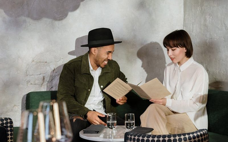 A couple sitting at a table in a stylish café choosing from the menu under a unique ceiling lamp.