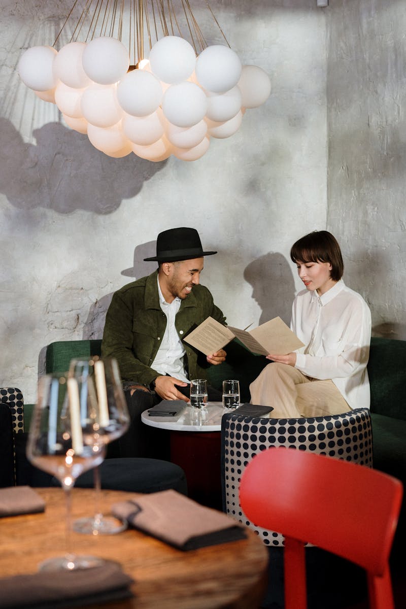 A couple sitting at a table in a stylish café choosing from the menu under a unique ceiling lamp.